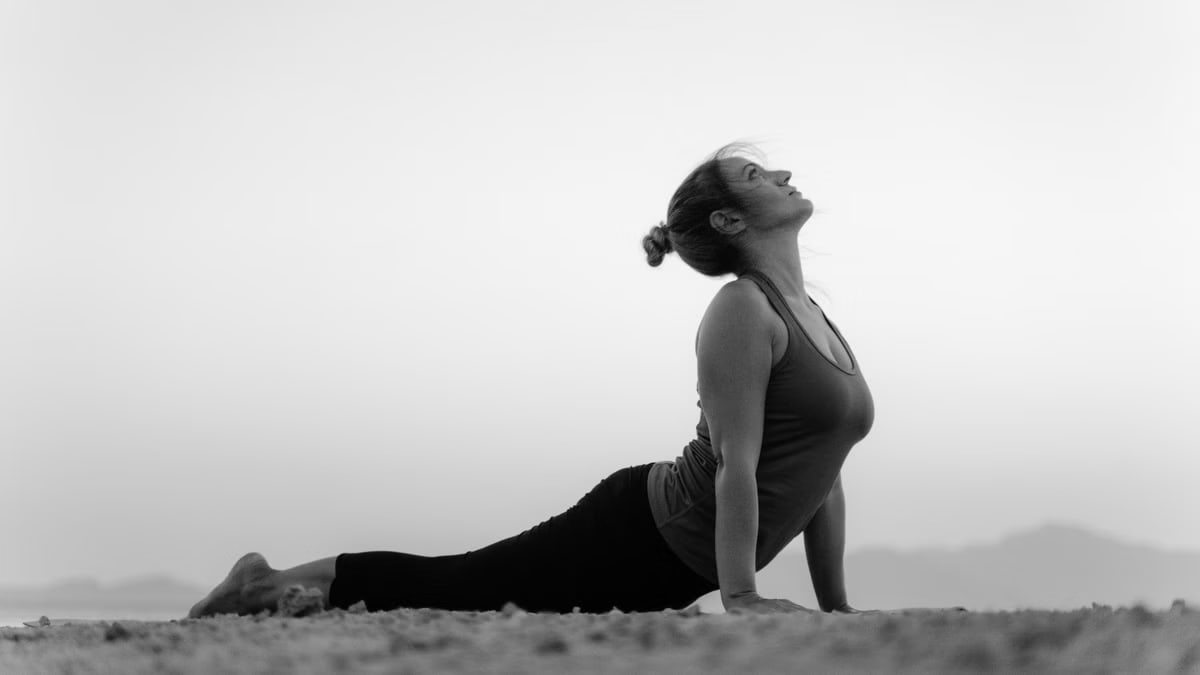 Black and white photo of a woman doing yoga's upward facing dog pose on a beach.
